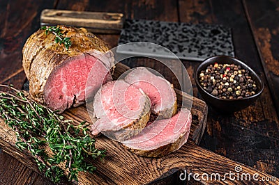 Roast Tenderloin beef fillet meat on a wooden board with herbs. Dark wooden background. Top view Stock Photo