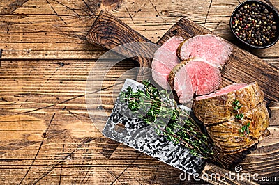 Roast Tenderloin beef fillet meat on a wooden board with herbs. Dark wooden background. Top view. Copy space Stock Photo