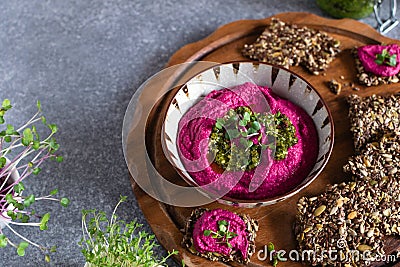 Roasted beet hummus in ceramic bowl, flax seed crackers on wooden cutting board, pesto sauce jar - vegetarian, vegan food concept Stock Photo