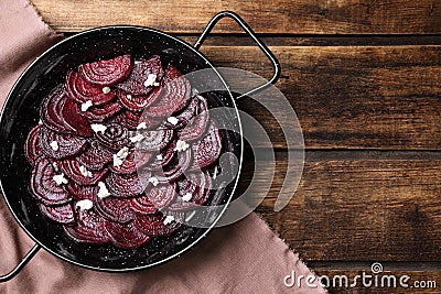 Roasted beetroot slices with feta cheese in wok pan on wooden table, flat lay. Space for text Stock Photo