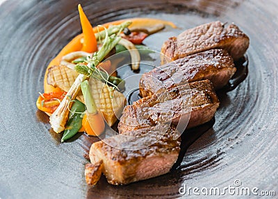 Roasted medium rare wagyu beef served with sour sauce with roasted baby vegetables on stone plate Stock Photo