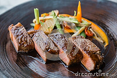 Roasted medium rare wagyu beef served with sour sauce with roasted baby vegetables on stone plate Stock Photo