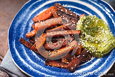 Roasted carrots and mashed avocado on a ceramic plate side view Stock Photo
