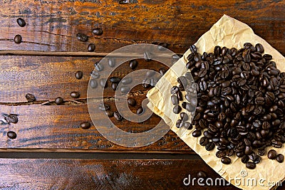 Roasted coffee beans on paper on rustic wooden table, beans around scattered Stock Photo