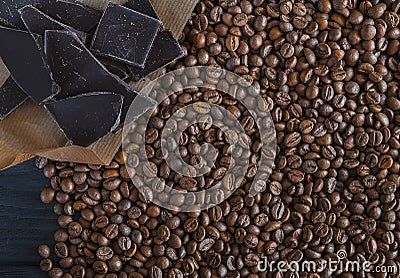 Roasted fragrant beans of black coffee are scattered on a black wooden table, on which black chocolate is lying Stock Photo