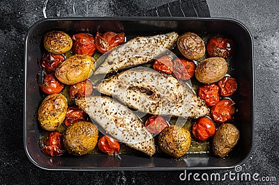 Roasted halibut fish steaks with tomato and potato. Black background. Top view Stock Photo