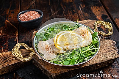 Roasted pollock or coalfish fish fillet served with green salad in a skillet. Wooden background. Top view Stock Photo