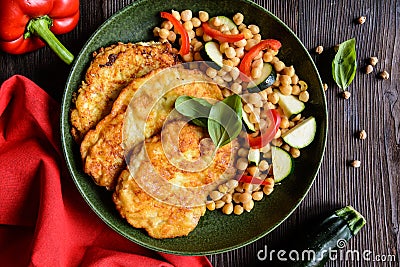 Roasted pork cutlets coated in cheese and breadcrumbs, served with chick peas and vegetable Stock Photo