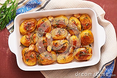 Roasted potatoes with garlic, thyme and rosemary in ceramic baking dish, top view Stock Photo