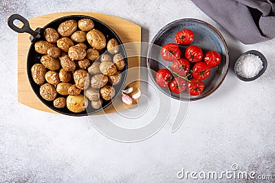 Roasted small whole potatoes in a cast iron skillet on concrete background. Top view, copy space, food background. Vegetarian or Stock Photo