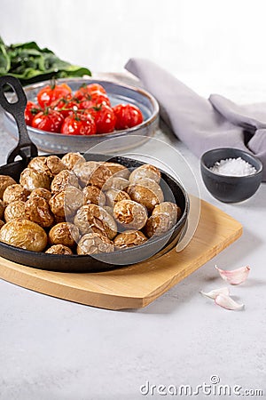 Roasted small whole potatoes in a cast iron skillet on concrete background. Vegetarian or vegan food concept Stock Photo