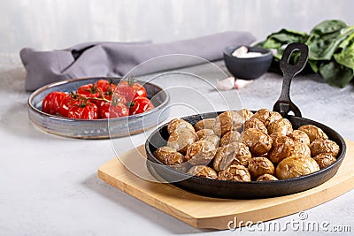 Roasted small whole potatoes in a cast iron skillet on concrete background. Vegetarian or vegan food concept Stock Photo