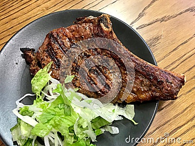 Roasted Veal Chop with Salad in Black Plate at Restaurant Stock Photo