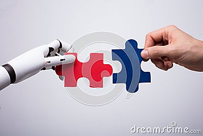 Robot And Human Hand Holding Jigsaw Puzzle Stock Photo