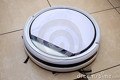 Robot vacuum cleaner working in the kitchen, sweeping debris from the tile floor Stock Photo