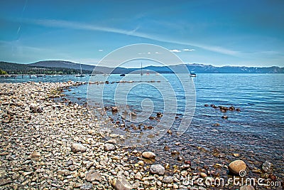 Rock beach at Lake Tahoe California with moored boats and dock and mountains in background Stock Photo