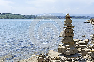 Rock cairn the art of stone balancing on a stone near a blue water flowing lake. Stock Photo