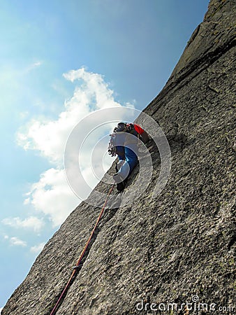 Rock climber dressed in bright colors on a steep granite climbing route in the Alps Stock Photo