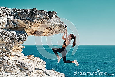 Rock climbing. Sport. Active lifestyle. Athlete woman hangs on sharp cliff. Seascape. Outdoors workout. High resilience Stock Photo