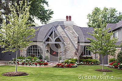 Rock house with American Flag plaque on arched front door and beautiful landscaping and sprinkler going Stock Photo