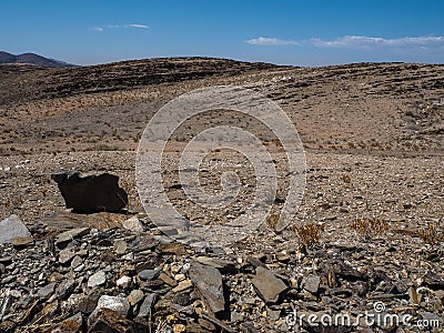 Rock mountain dried dusty landscape ground of Namib desert with splitting shale pieces, other stone, desert plant and blue sky Stock Photo
