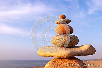 Rock zen pyramid of multi-colored pebbles in the pink rays of the setting sun against the sea. Peace of mind concept Stock Photo