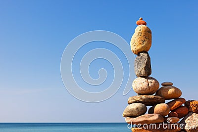 Rock zen pyramid of white and pink pebbles on a background of blue sky and sea Stock Photo
