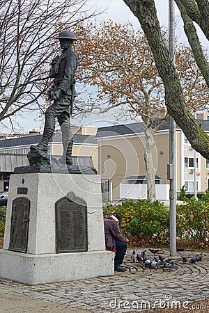 Rockaway Park, Queens, New York: An old man feeds pigeons beneath a statue Editorial Stock Photo