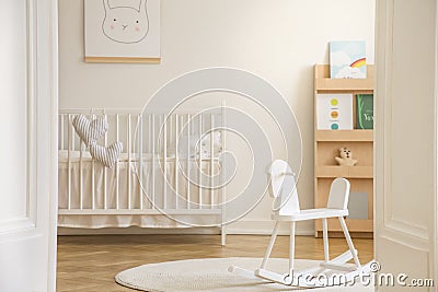 Rocking horse on rug in white kid`s bedroom interior with rabbit poster above cradle Stock Photo