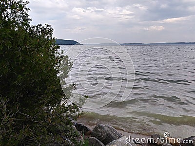 Rocks Lake trees pebbles waves water sky clouds vegetation beach evening view scenic Stock Photo