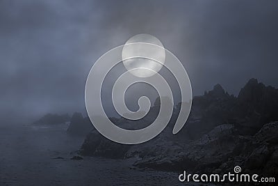 Rocky coast in a foggy full moon night Stock Photo