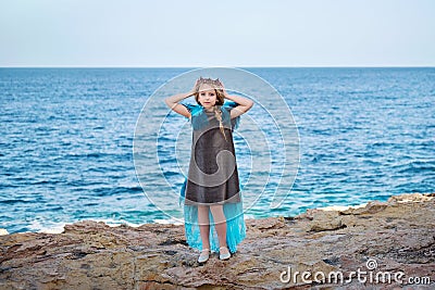 On a rocky seashore young girl princess skyblue dress like a bird queen puts on a crown Stock Photo