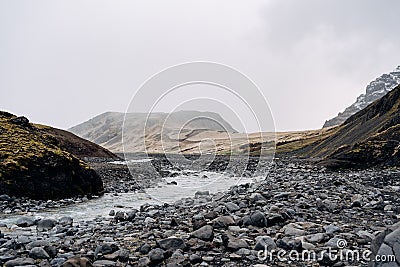 Rocky shallow mountain river in Iceland, flows against the backdrop of mountains. Stock Photo