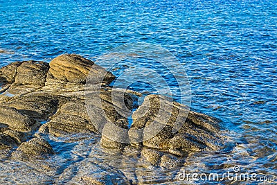 Rocky shore line scenic view waterfront blue water with evening orange lighting on stones Stock Photo