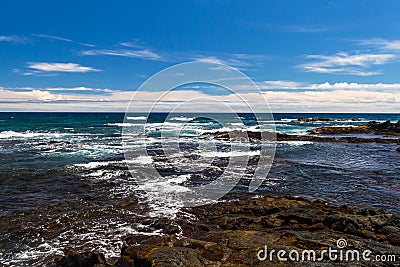 Rocky shoreline, Black Sand Beach, Hawaii. Rocks, blue ocean and waves; blue sky, clouds in background. Stock Photo