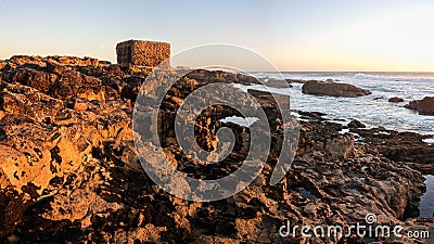 Rocky shoreline in front of a wavy sea under the sunlight during sunset in Portugal Stock Photo
