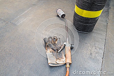 Roll of bituminous sheath, propane torch and glove resting on a bituminous membrane already laid Stock Photo