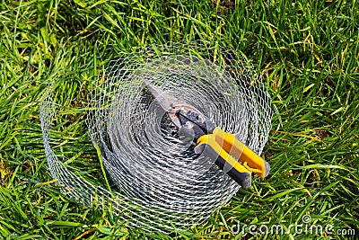 A roll of reinforced mesh for construction and wire cutters lie on the grass. Horticultural use to protect the roots of the Stock Photo