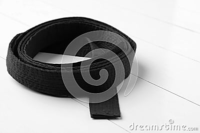 Rolled black belt on white wooden background, closeup. Oriental martial arts Stock Photo