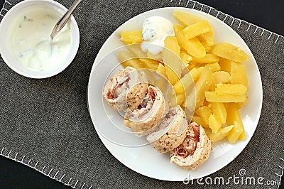 Rolled chicken fillet with prosciuto and mozzarela with pototoes on white plate on grey cloth Stock Photo