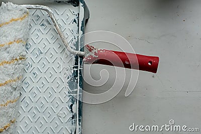 Roller with a red handle in a green pallet with white paint. Stock Photo