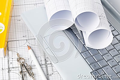 Rolls of architectural blueprint house building plans on laptop computer keyboard with pencil, compasses and level Stock Photo