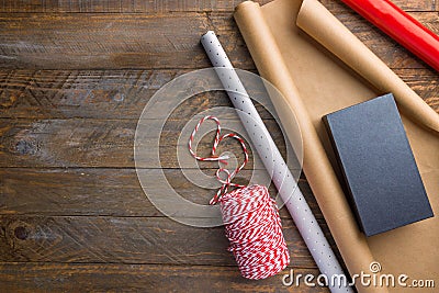 Rolls of different brown Kraft red silver wrapping paper striped ribbon gift box on wood table. Christmas New Year holiday present Stock Photo