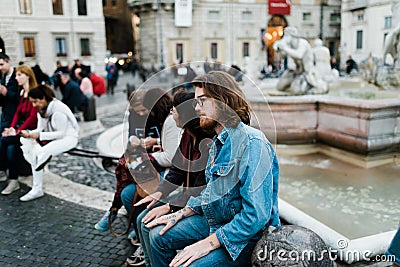 Roma, Italy, November 1, 2015: A group of young tourists sitting at an urban fountain Editorial Stock Photo