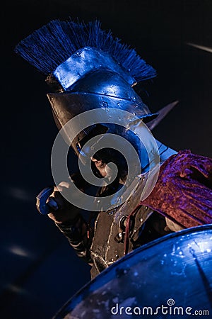 Roman legionnaire in armor with a sword and shield on a black background. The face is hidden by a helmet. Stock Photo