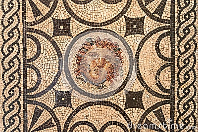 Close-up on roman mosaic portraiting a chubby medusa face surrounded by ancient decorative pattern Stock Photo