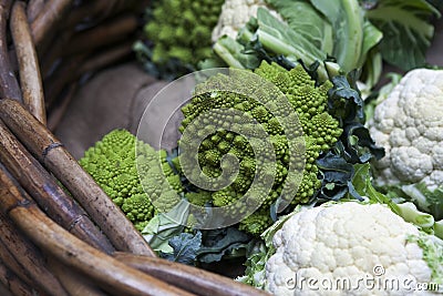 Romanesco cauliflower with its fractal shapes and Fibonacci sequences in focus, and cabbage leaves in the background. Stock Photo