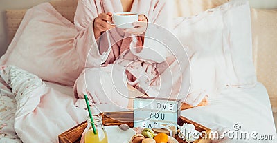 Romantic Breakfast in bed with I love you text on lighted box, macaroons, gift box on tray and blurred cropped woman in a bathrobe Stock Photo