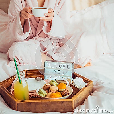 Romantic Breakfast in bed with I love you text on lighted box, macaroons, gift box on wooden tray and blurred cropped woman in a Stock Photo