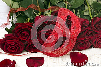 Romantic carnival concept. Red carnival mask and bouquet of red roses on light wooden background. Close-up Stock Photo
